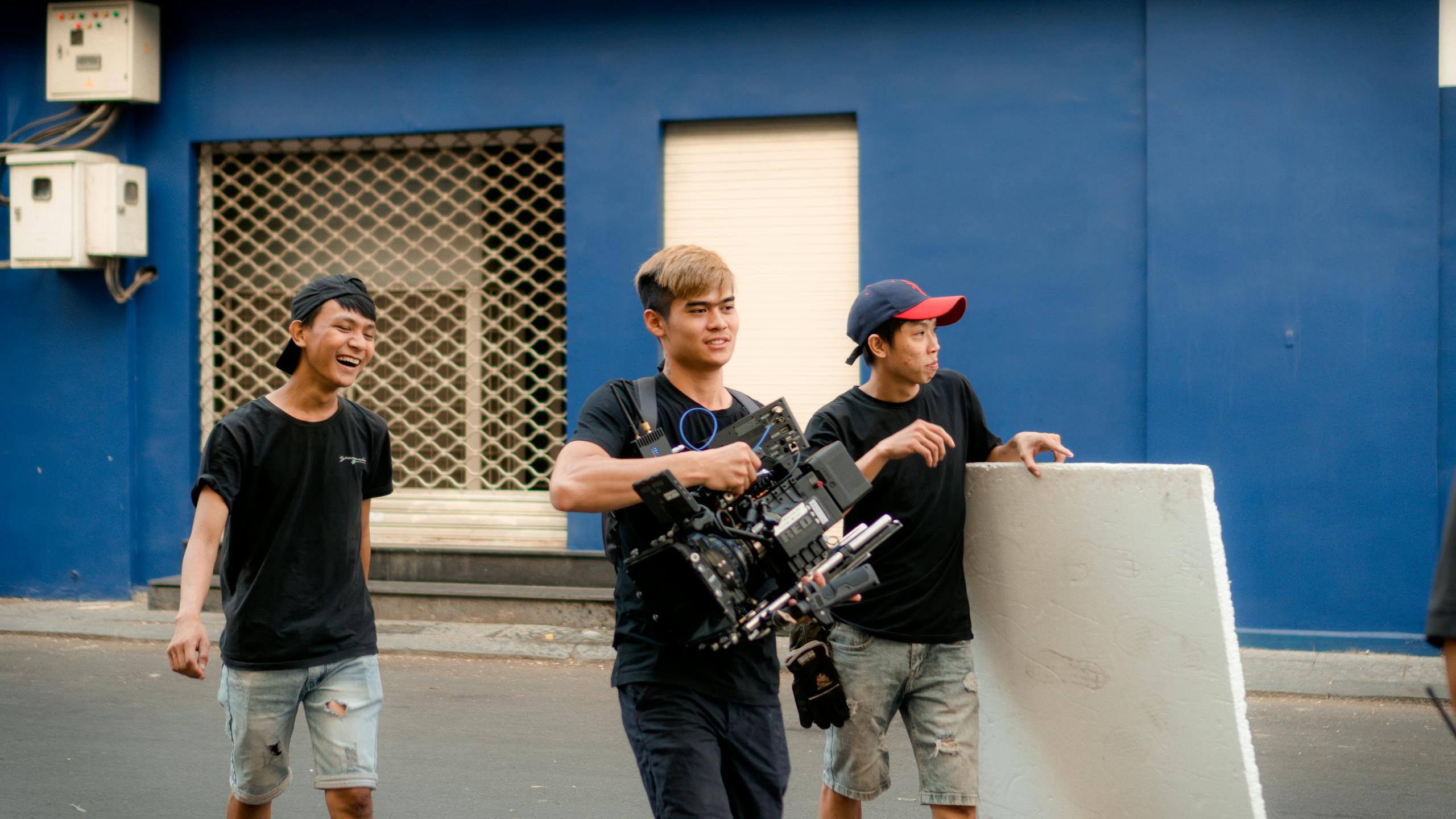 A camera crew of three men filming outdoors on an urban street with equipment.
